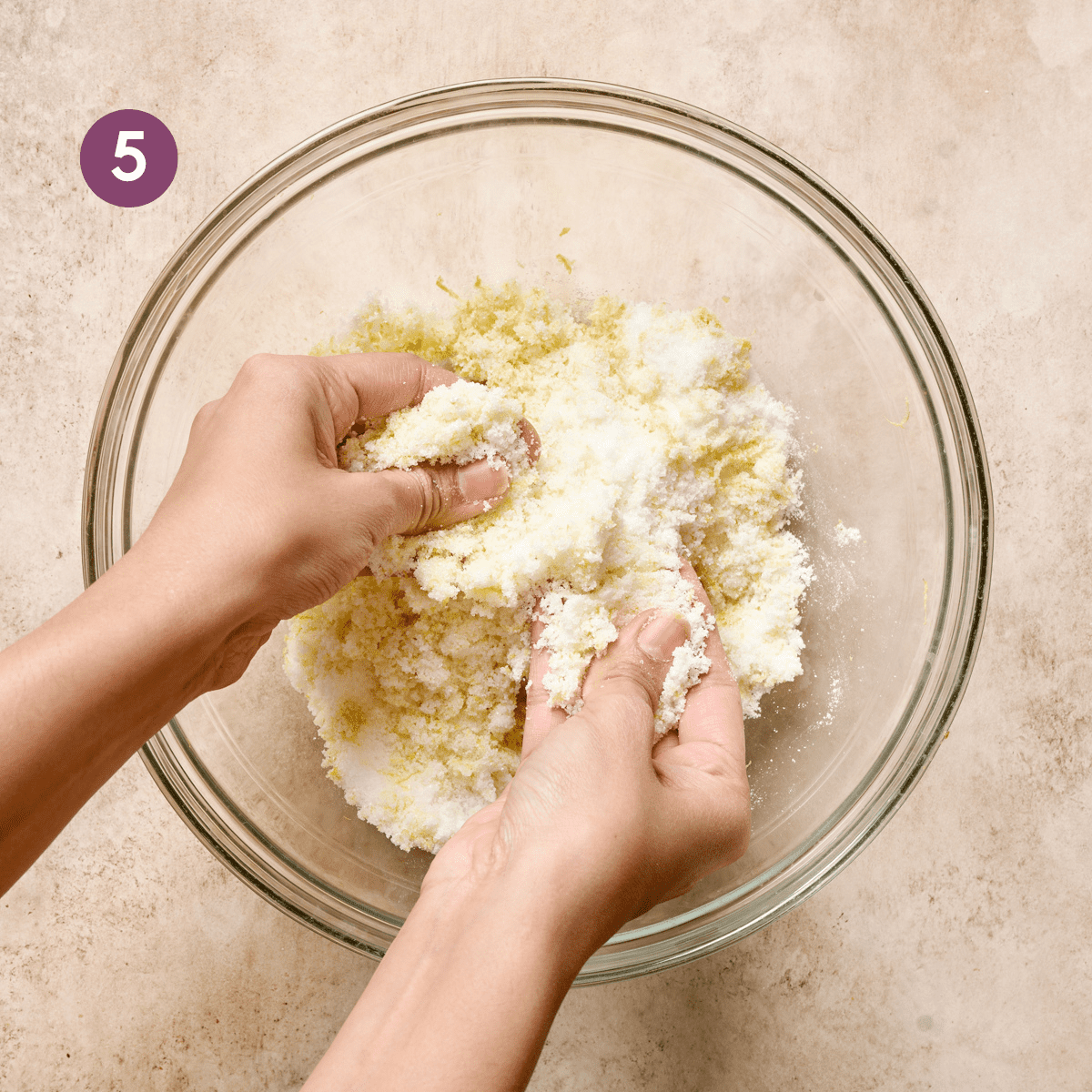 woman's hands massaging lemon zest into sugar in a glass bowl for a vegan lemon cake.
