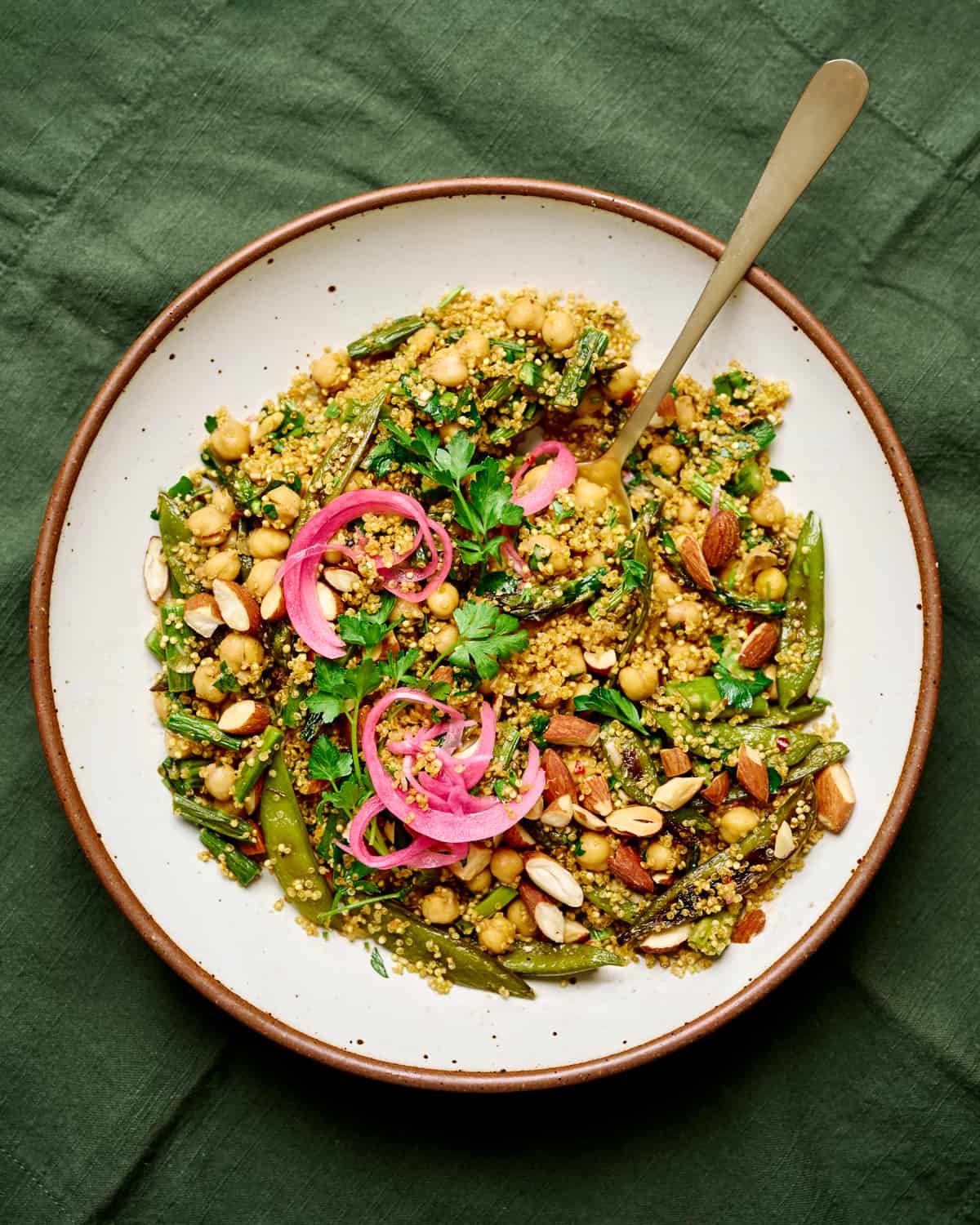 Large white plate with a spoon and quinoa salad topped with pickled onions.