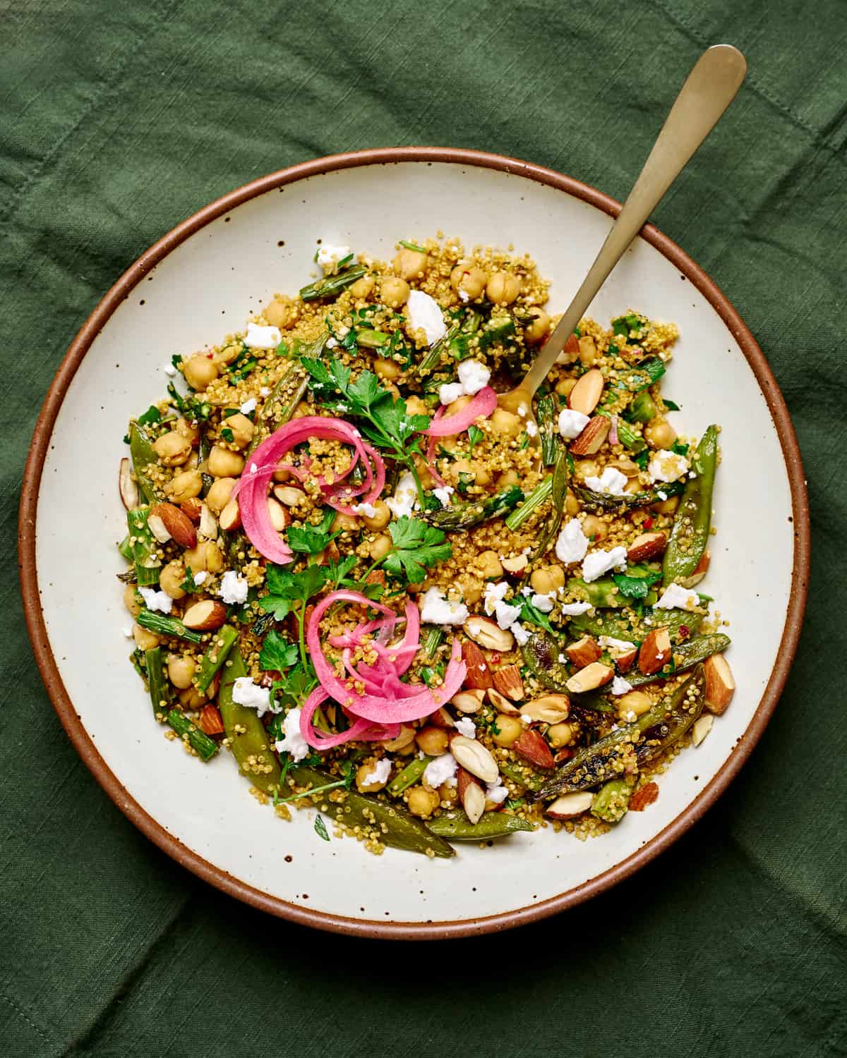 Round white plate with a spoon and quinoa salad topped with vegan feta and pickled onions.