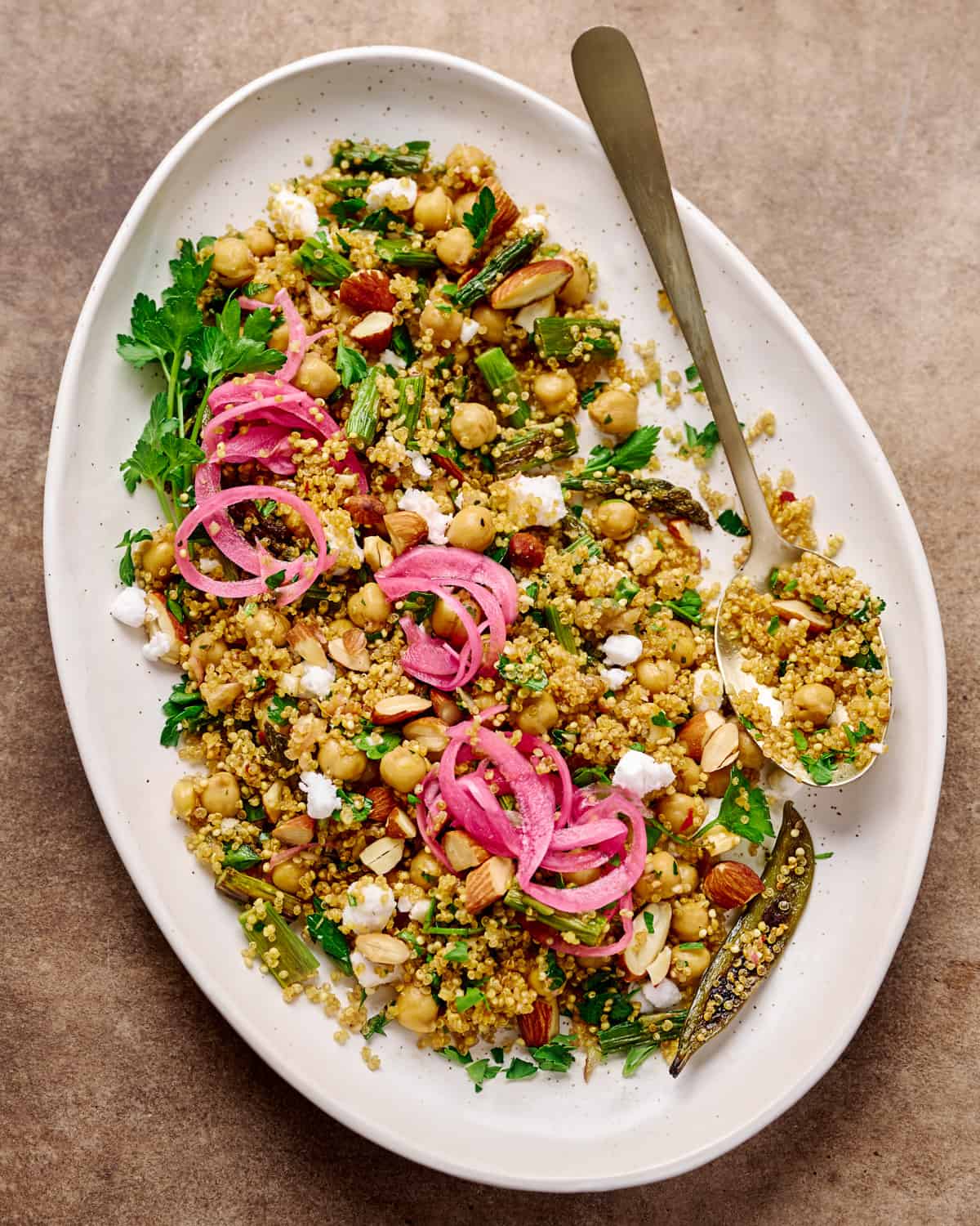 Large white plate with a spoon and quinoa salad topped with vegan feta and pickled onions.