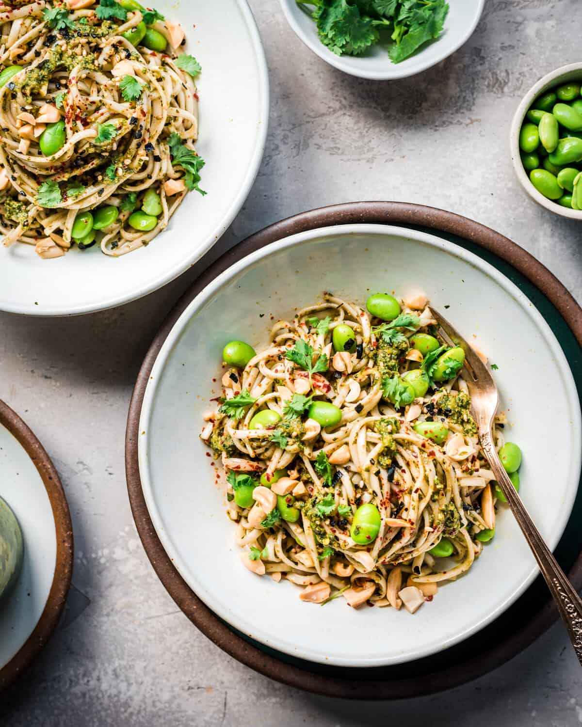 Two bowls of Thai pesto pasta with edamame on a grey table.