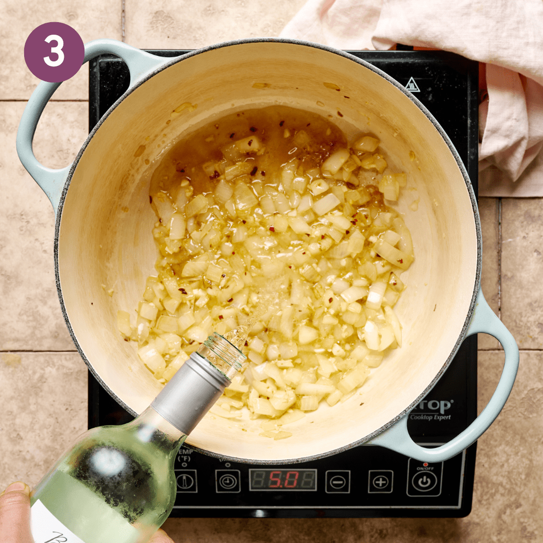 Person adding white wine into garlic onion mixture in pot.