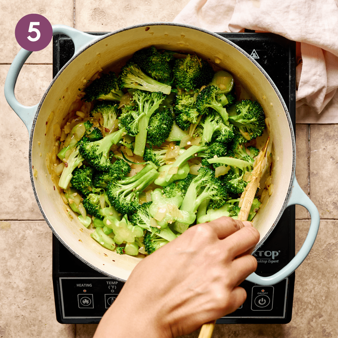 Person stirring broccoli that was just added to the pot.