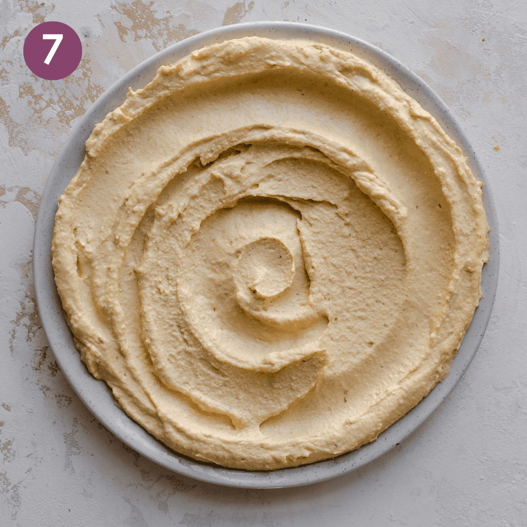 Wavy hummus on a large white serving plate.