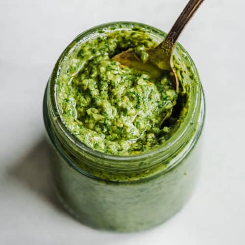 Overhead view of spoon in a small glass jar filled with pesto.