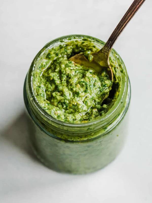 Overhead view of spoon in a small glass jar filled with pesto.