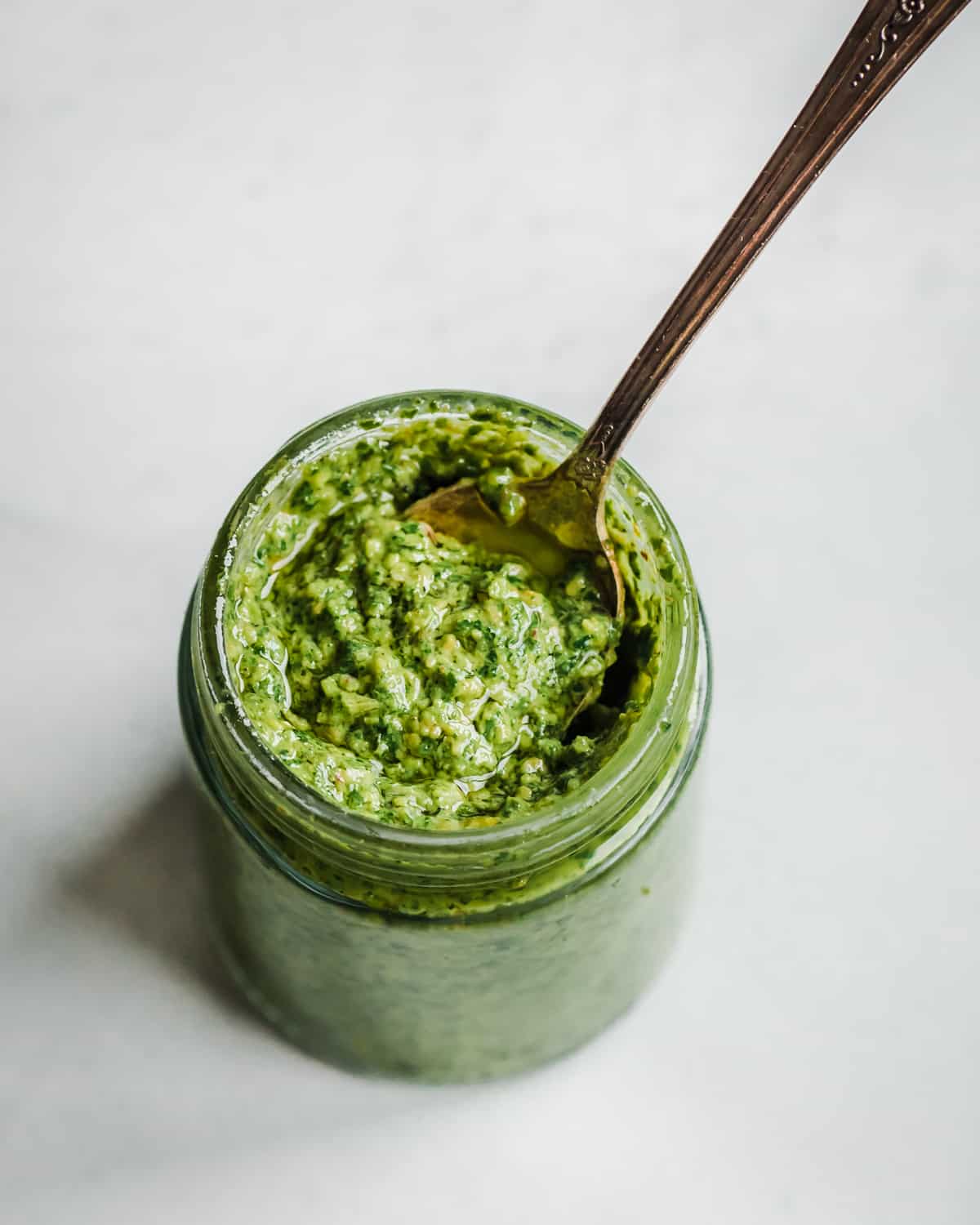 Overhead view of a small glass jar with pesto and a spoon in it.