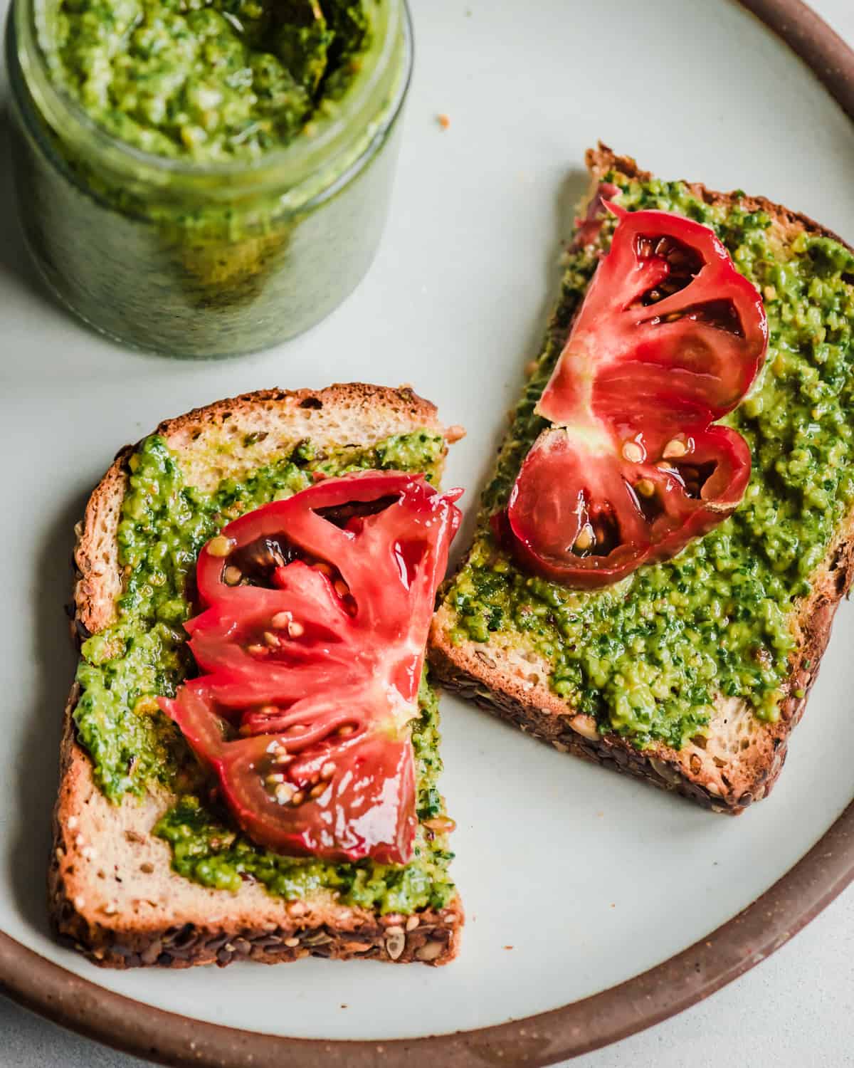 Vegan pesto and heirloom tomatoes on two halves of a piece of toast.