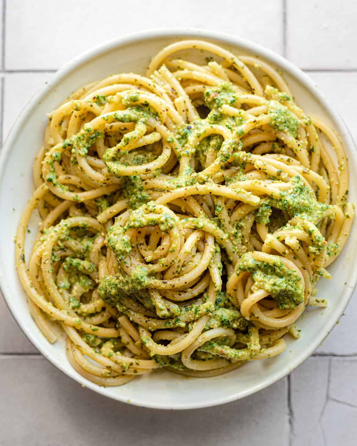 Overhead view of pesto covered spaghetti on a white plate.