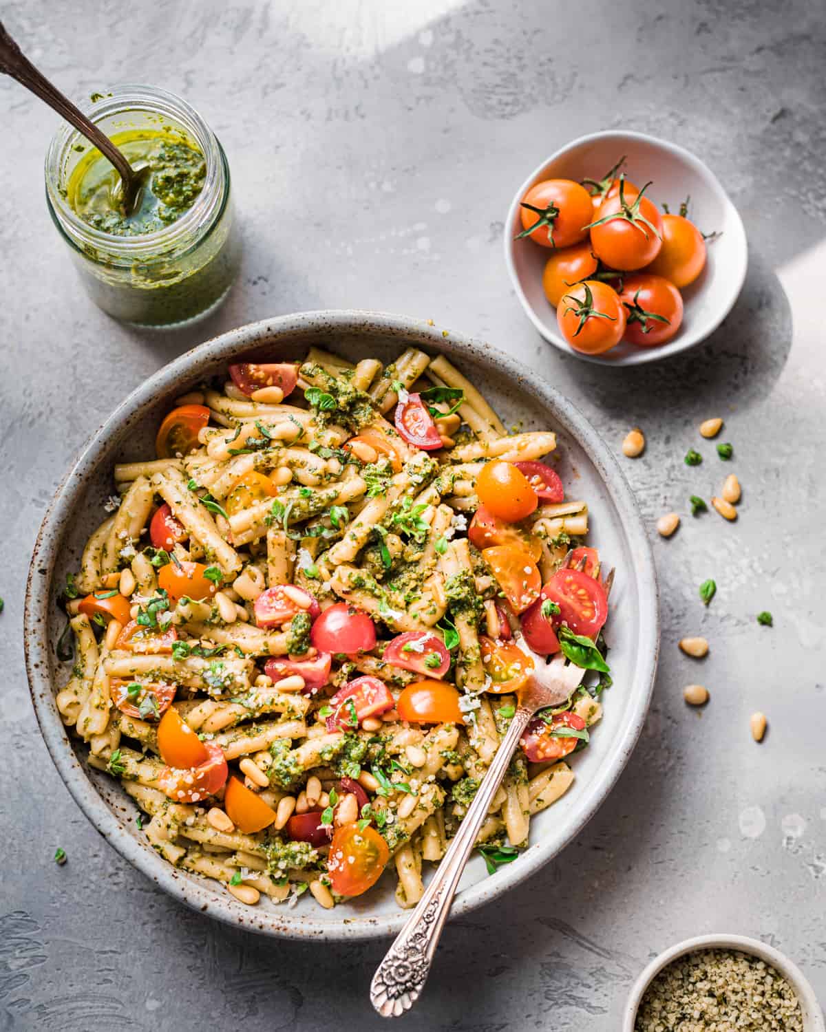 Overhead view of pesto pasta with tomatoes in a bowl on a grey table.