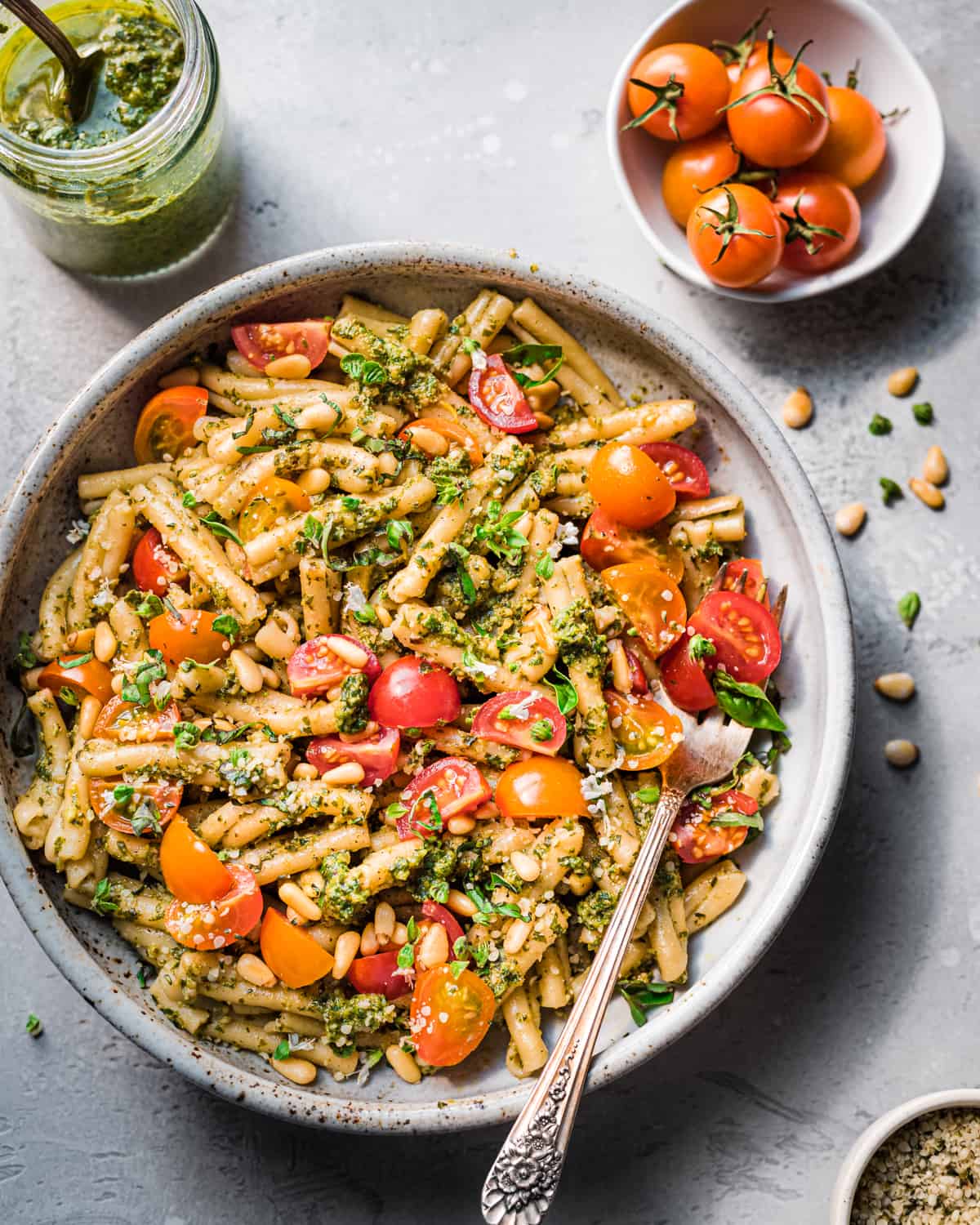 Overhead view of pesto pasta with tomatoes in a bowl on a grey table.