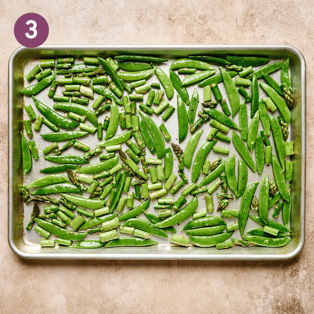 Sliced asparagus and snap peas covered in oil, salt and pepper on a baking sheet.