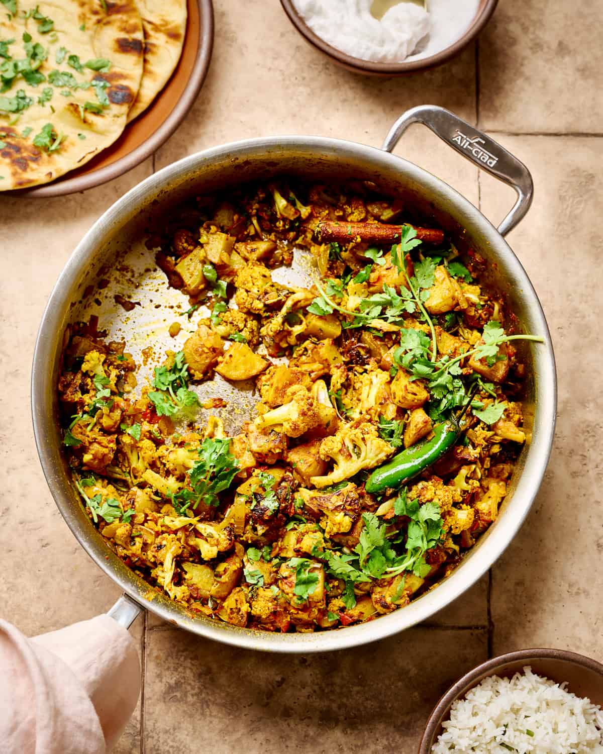 Overhead view of aloo gobi in a deep sauté pan on a brown table.