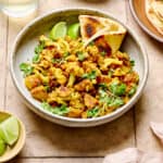 Aloo Gobi with naan in a white bowl on a light brown tiled table.