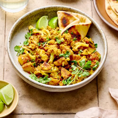 Aloo Gobi with naan in a white bowl on a light brown tiled table.