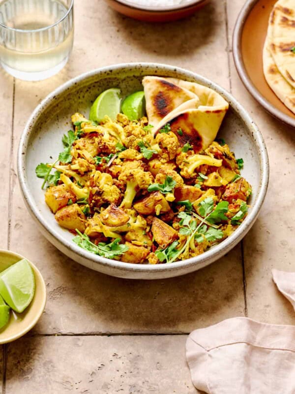 Aloo Gobi with naan in a white bowl on a light brown tiled table.
