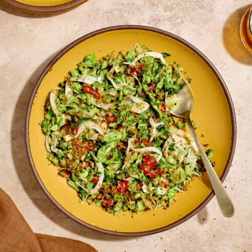 Overhead view of broccoli salad and a serving spoon on a yellow plate on a table.