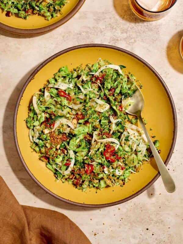 Overhead view of broccoli salad and a serving spoon on a yellow plate on a table.