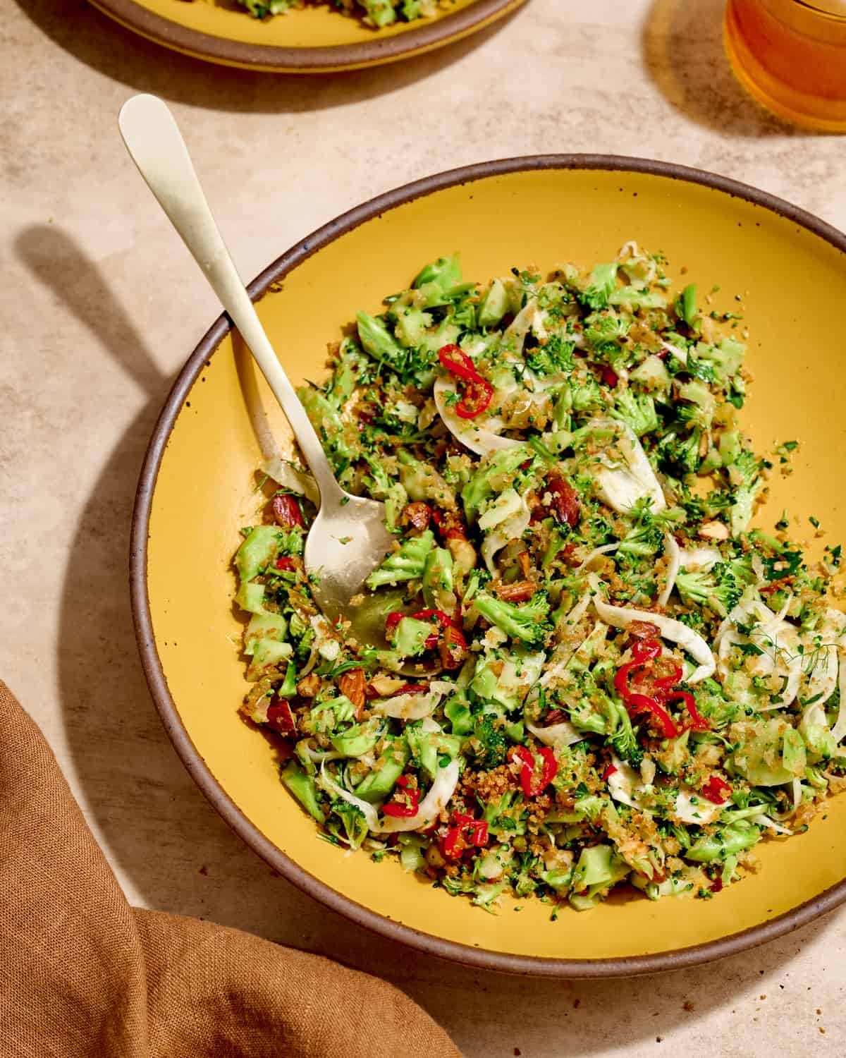 Overhead view of plate of broccoli salad with a serving spoon on a cream table.