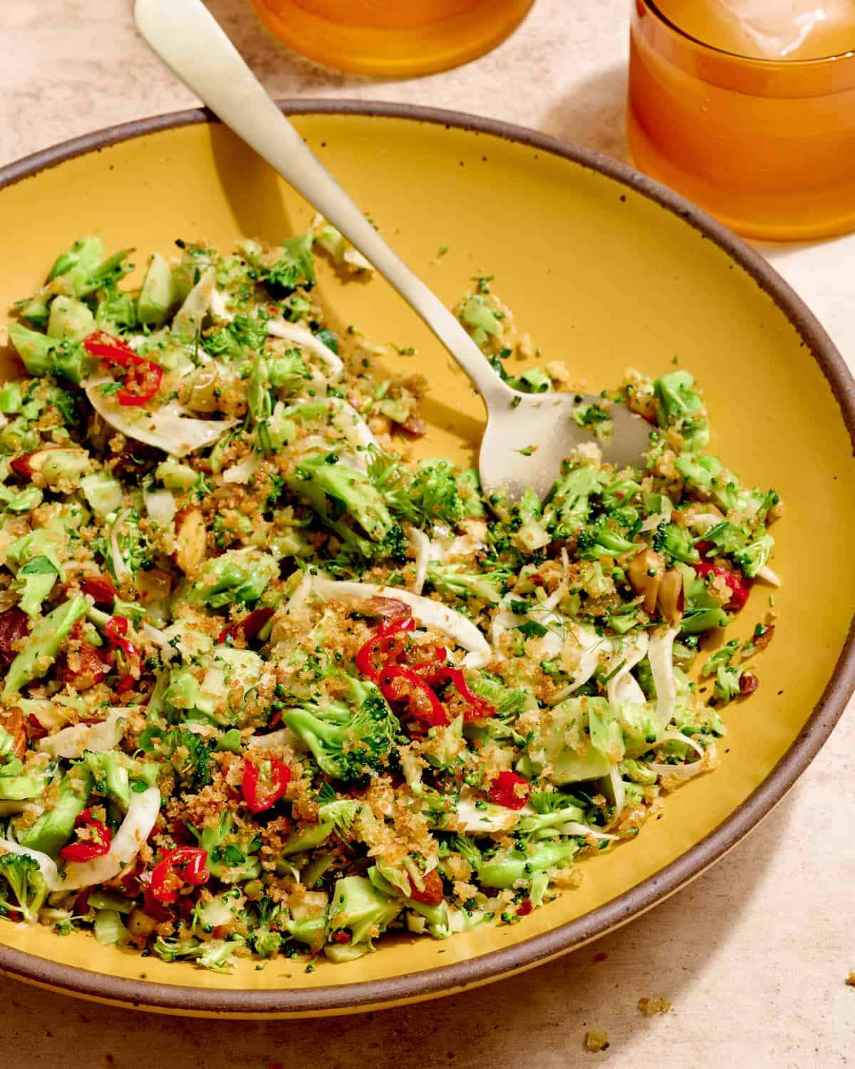 Close up side view of plate of broccoli salad on a yellow plate on a cream table.