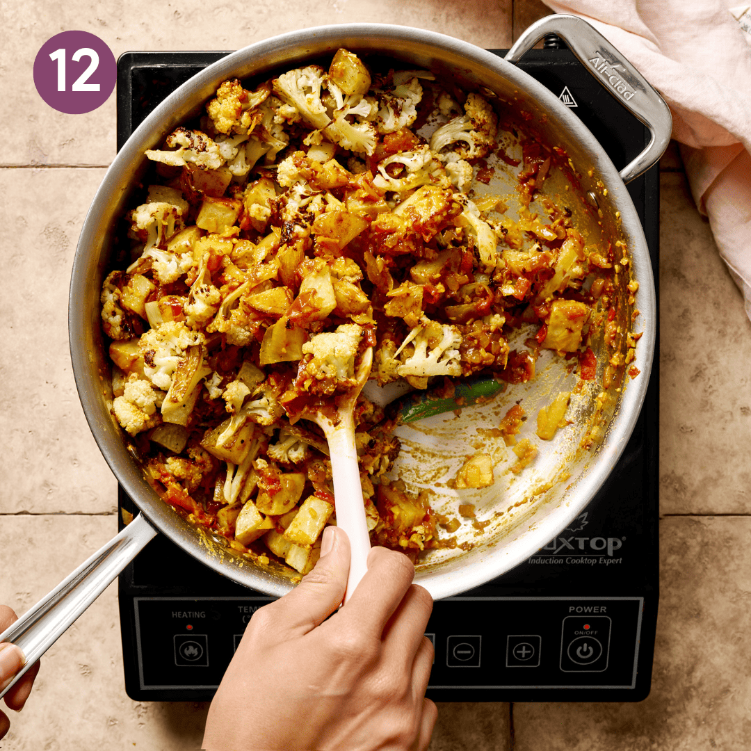 Person mixing the potatoes and cauliflower into the rest of the ingredients in the pan.