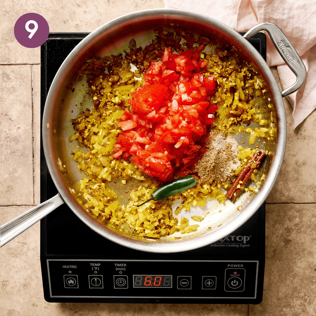 Amchur, coriander, chile powder, serrano pepper, tomatoes, salt, and pepper added to aromatics in pan.