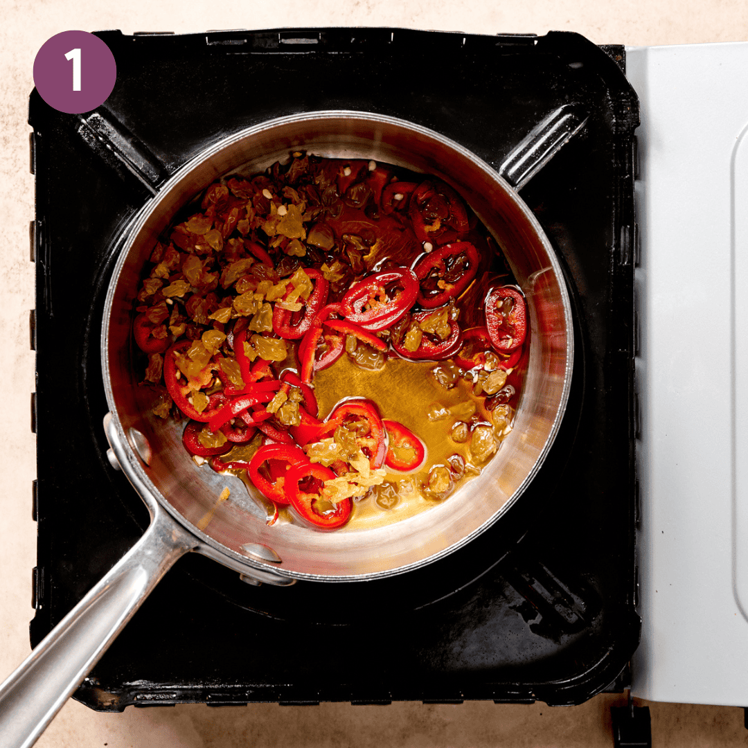 Peppers, raisins and maple syrup in a saucepan on a stovetop.