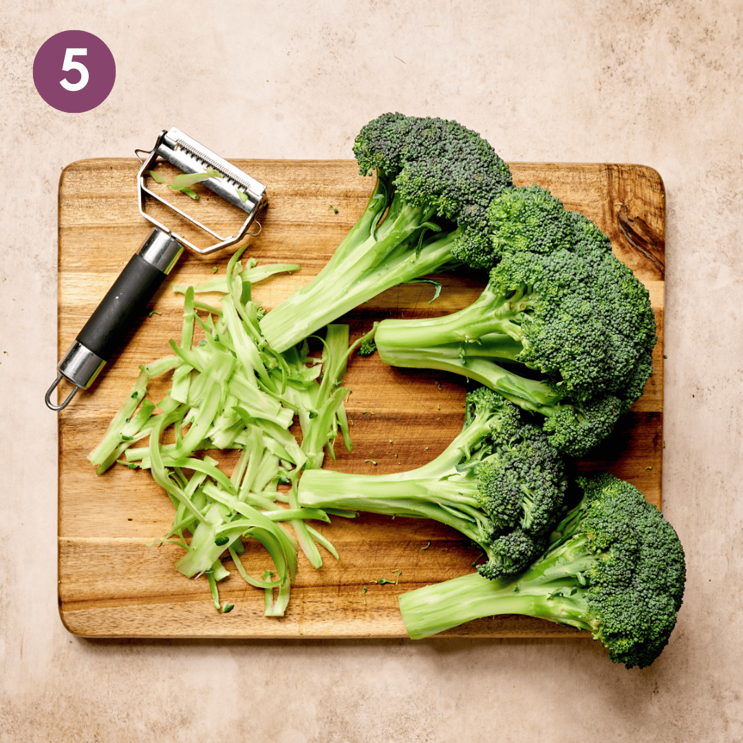 Stalks peeled off of 3 crowns of broccoli on a wooden cutting board.