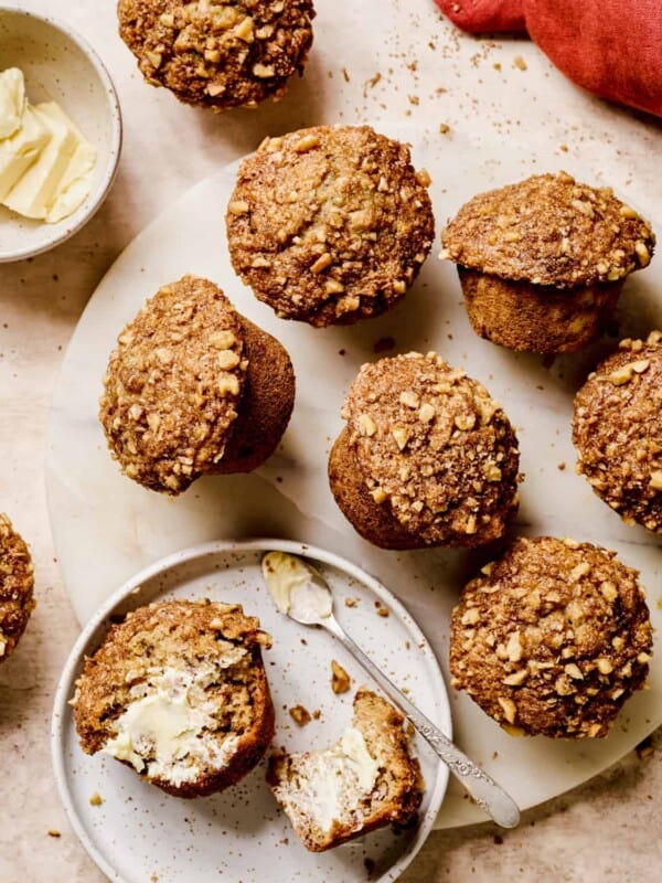 Baked banana muffins on a serving platter with one muffin sliced open and buttered.