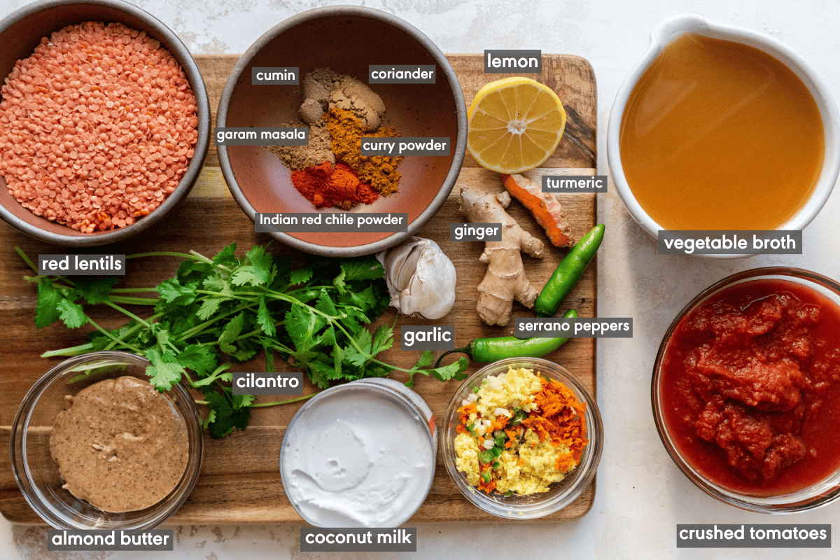 Red lentil curry ingredients in various bowls on a wooden cutting board.
