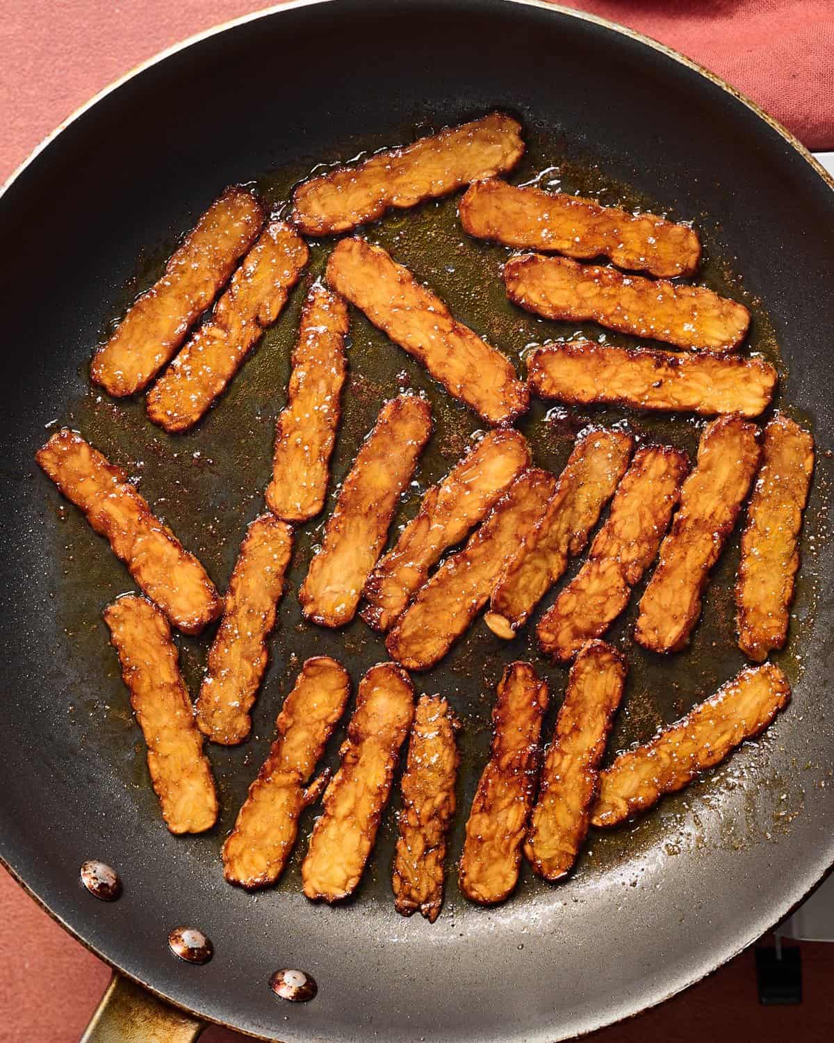 Cooked tempeh bacon slices in a pan.