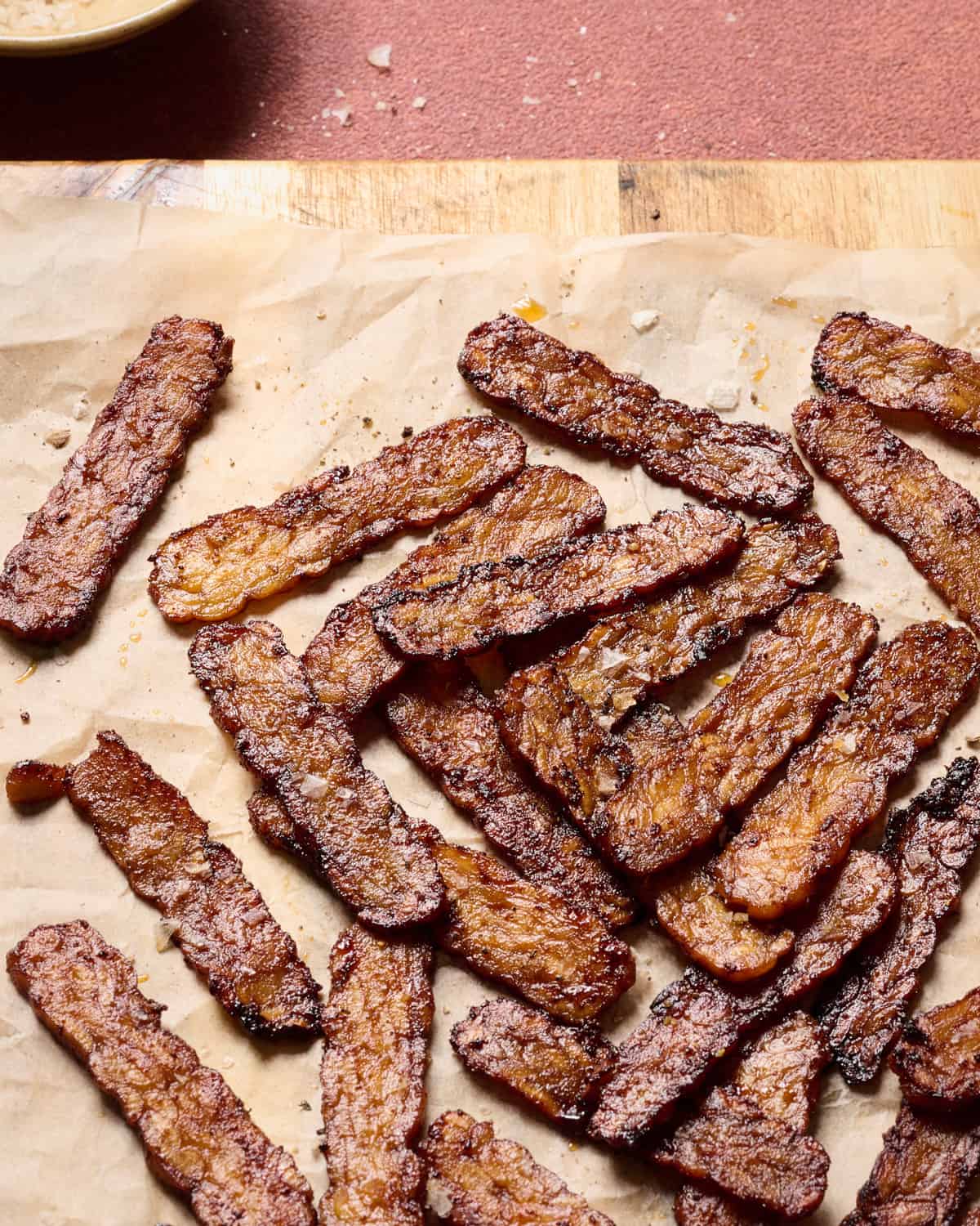 Tempeh bacon slices on a piece of parchment paper.