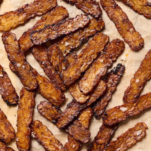 Crispy browned tempeh bacon slices on a piece of parchment paper.