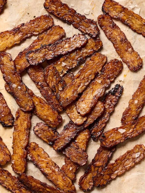 Crispy browned tempeh bacon slices on a piece of parchment paper.