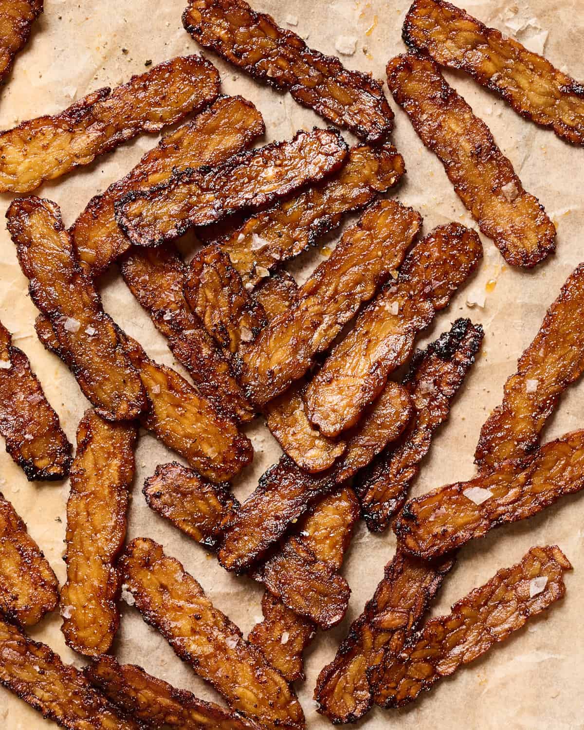 Crispy browned tempeh bacon slices on a piece of parchment paper.