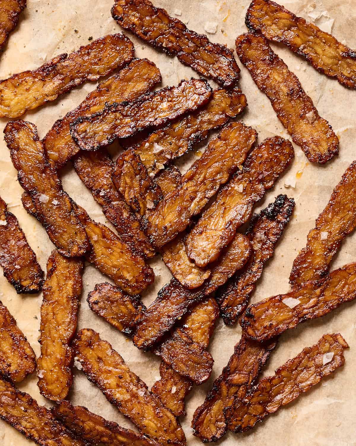 Tempeh bacon slices on a piece of parchment paper.