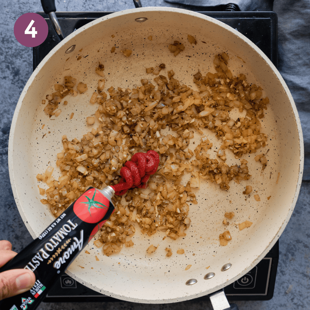 person adding tomato paste to onions in pan.