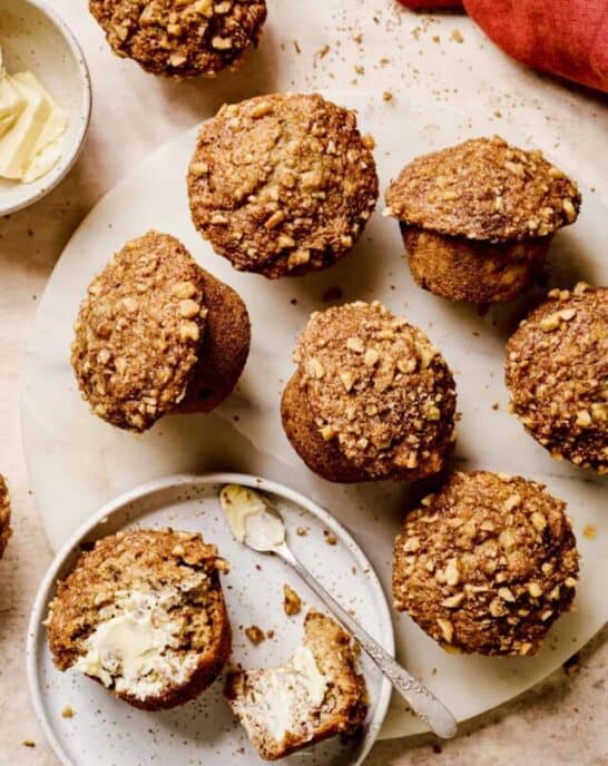 Baked banana muffins on a serving platter with one muffin sliced open and buttered.