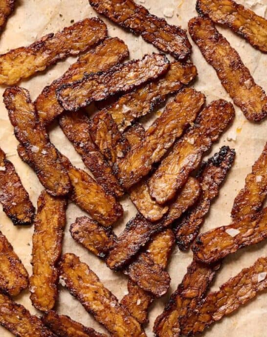 Crispy browned tempeh bacon slices on a piece of parchment paper.