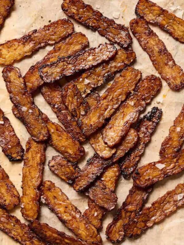 Crispy browned tempeh bacon slices on a piece of parchment paper.