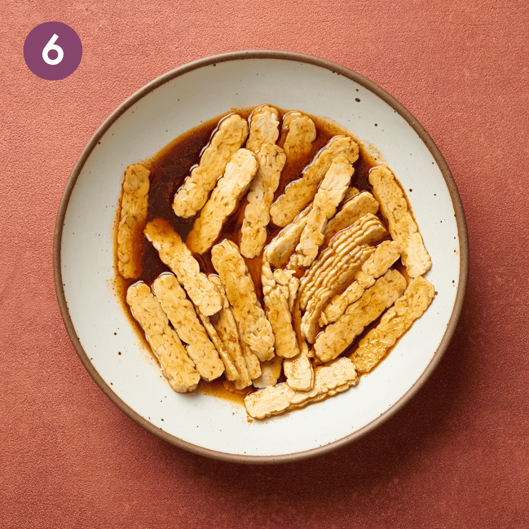 Tempeh strips and marinade mixed in the large bowl.