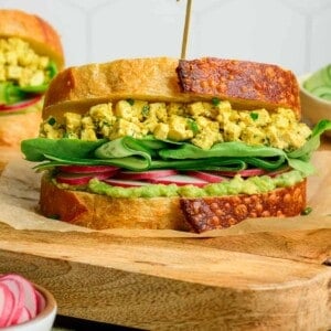 side view of egg salad sandwich on a wooden cutting board.