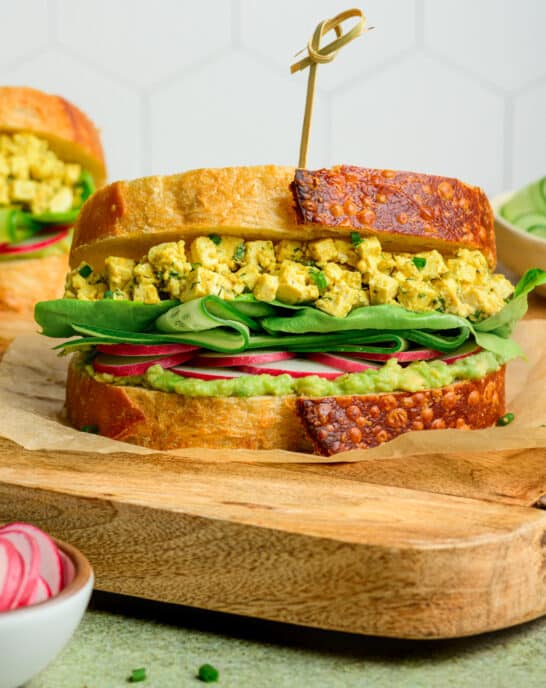 side view of egg salad sandwich on a wooden cutting board.