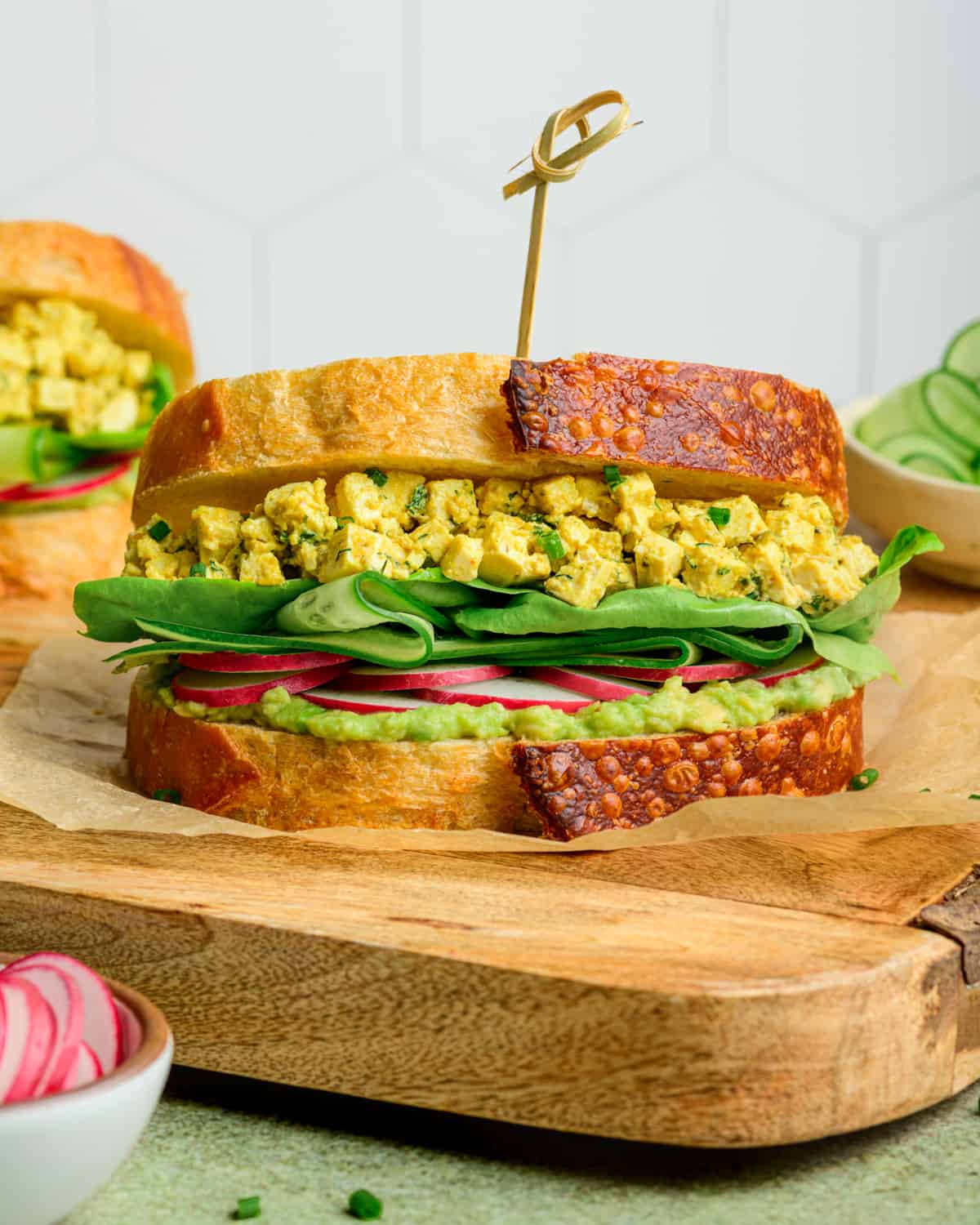 Side view of vegan egg salad sandwich on a wooden cutting board.