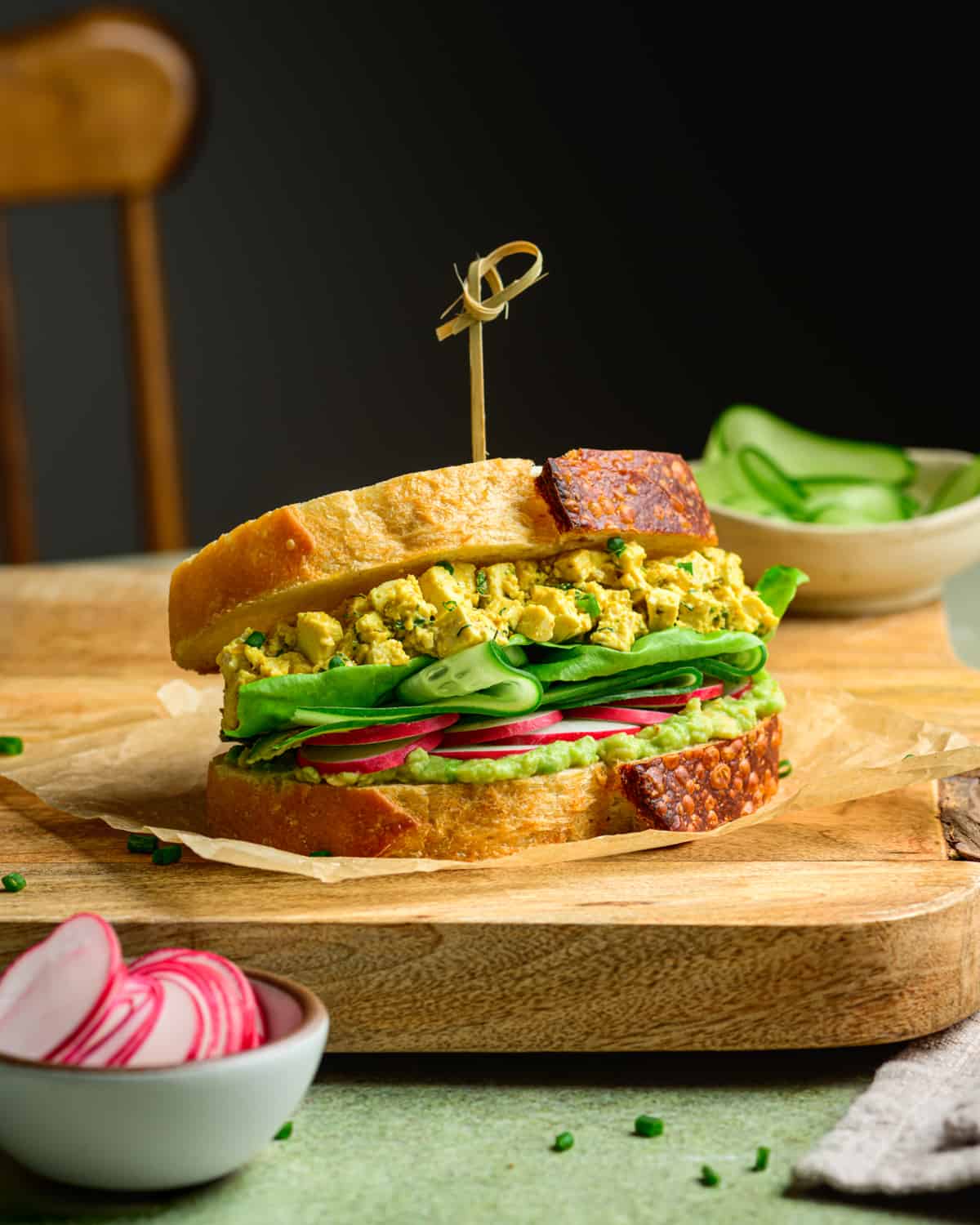 Vegan egg salad sandwich on a wooden cutting board on a table.