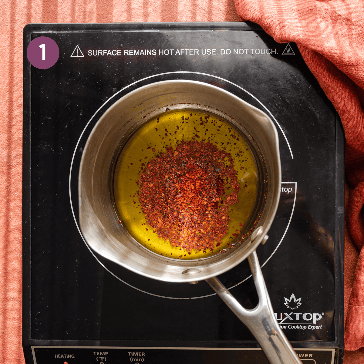 red chili flakes and olive oil in a stainless steel saucepan on a cooktop.