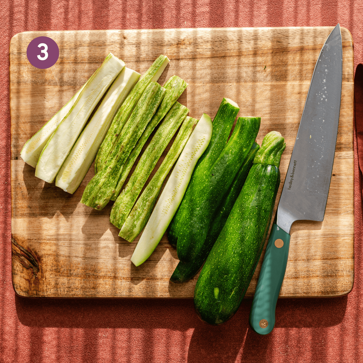 Zucchini sliced lengthwise and arranged on a wooden cutting board with a knife.