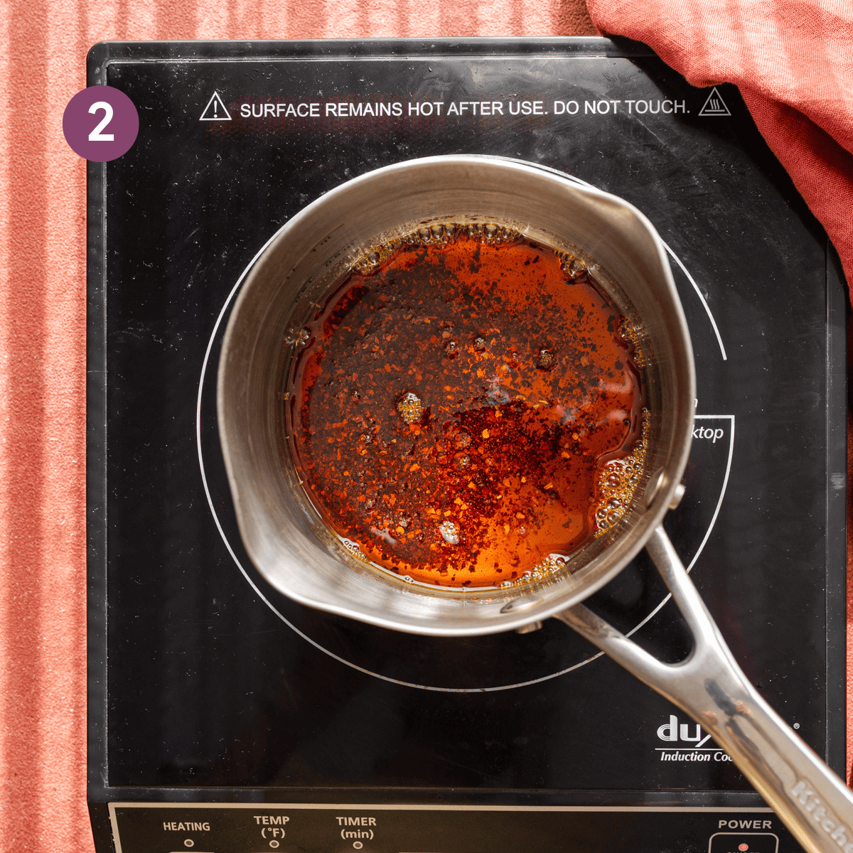 red chili flakes and olive oil simmering in a stainless steel saucepan for chili oil.