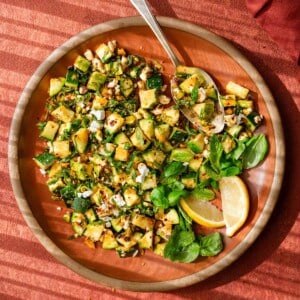 zucchini salad tossed with chili oil, pistachios, feta, basil, and mint on a red place on a red surface.