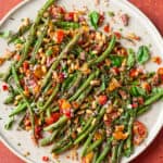 Overhead view of plate of charred green beans on a red table.